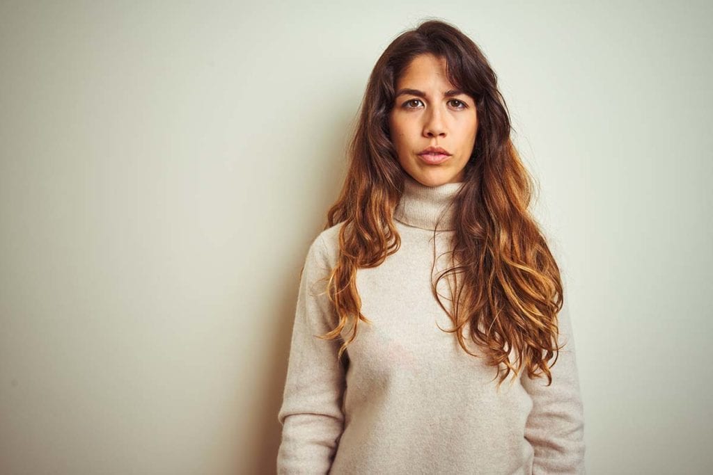 woman standing against wall looking serious about common relapse triggers