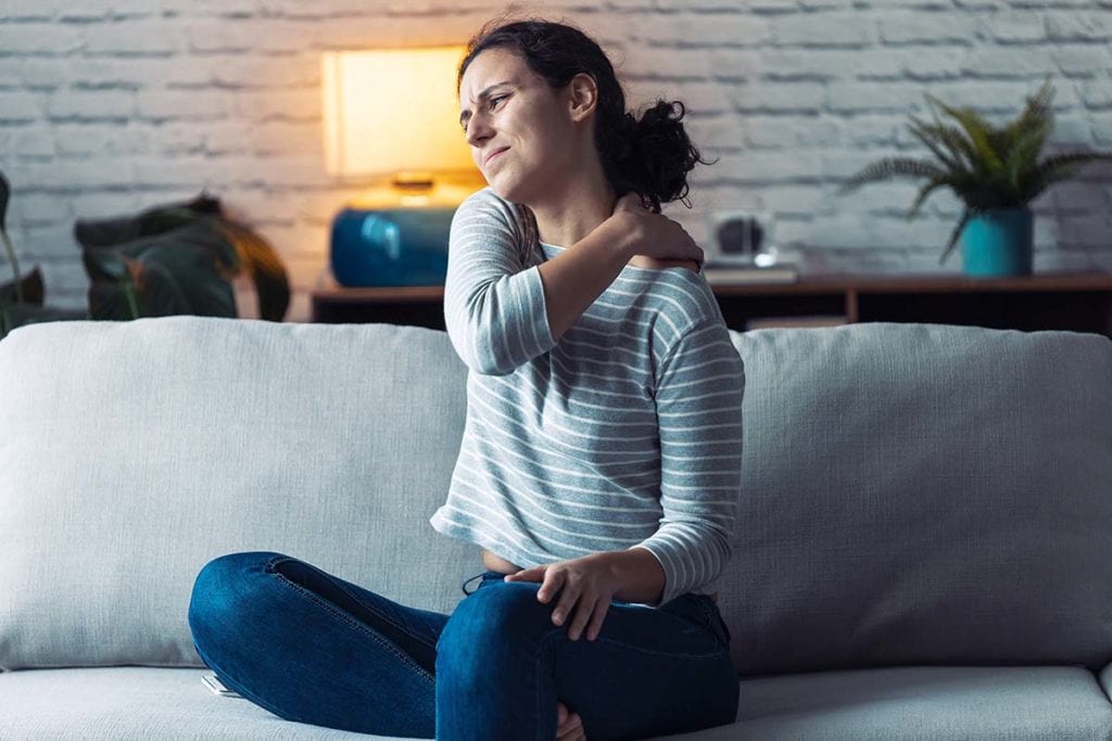 woman sitting on couch stretching with aches from coping with opioid withdrawal