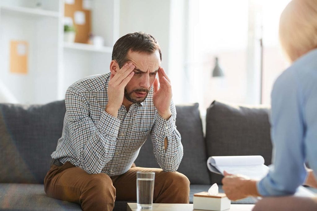 man on couch holding temples surprised by stages of alcoholism