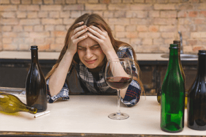 woman with hands on head and wine bottles, substance use disorder