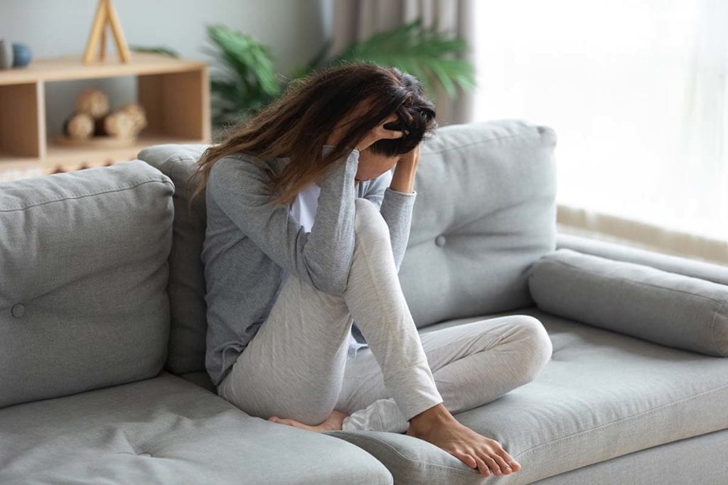 woman on couch with hands on head stressing about types of addiction