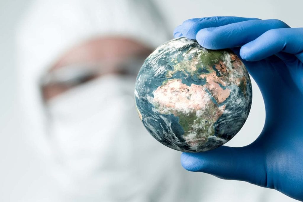 man in protective antidisease gear holds a miniature globe to represent epidemic vs pandemic