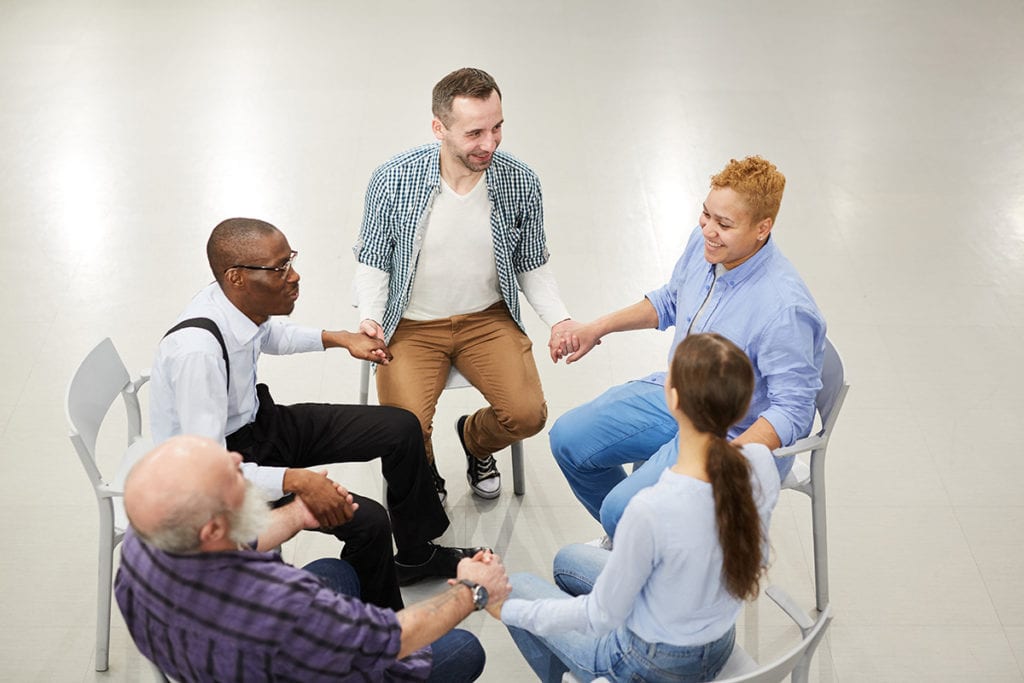 group therapy circle discusses substance abuse preventions while all holding hands