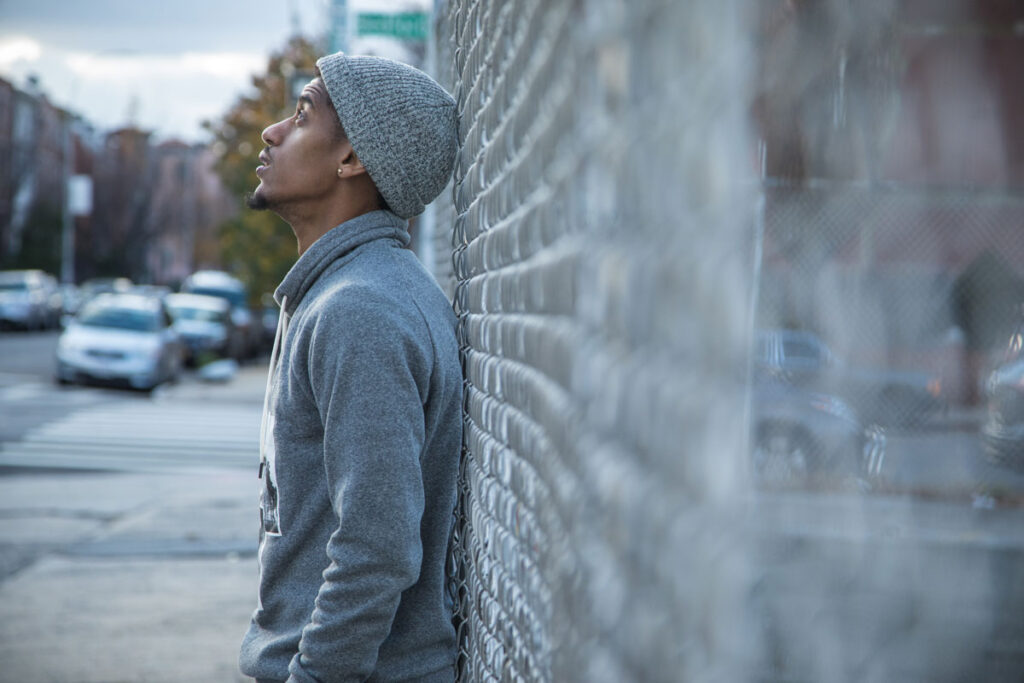 A mean leans against an outside wall. He stares up at the sky and wonders why he can't stop taking Liquid G.