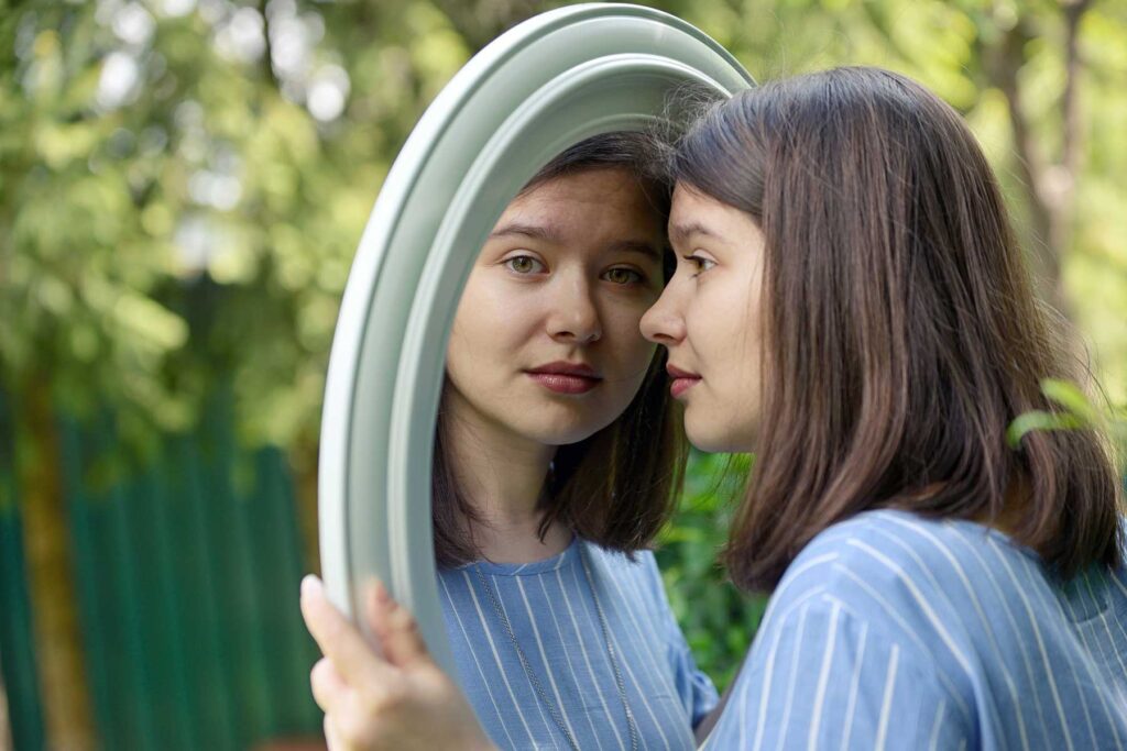 Woman looking into mirror at her reflection and thinking about moral inventory and recovery from addiction