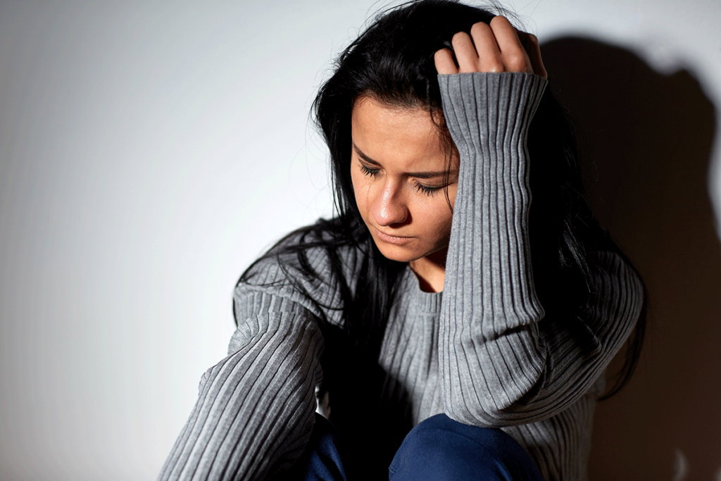a distressed woman holds her hand to her head thinking about the connection between depression and addiction
