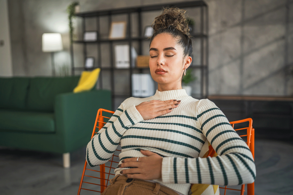woman in strip shirt holds her palms to her chest and stomach while learning about how to calm an anxiety attack