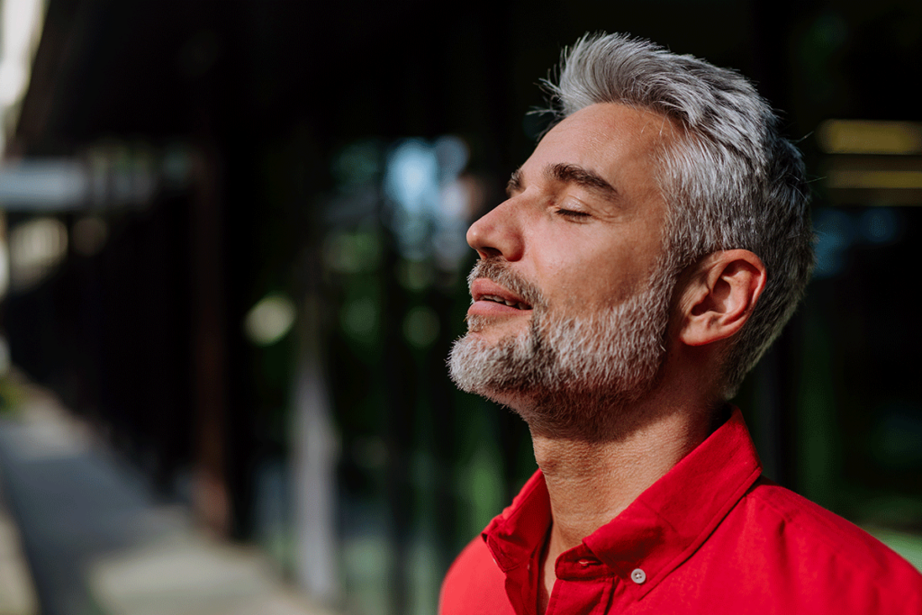 man with gray hair and beard closes his eyes and looks up to the sun and thinks how great it feels to finally begin his healing from trauma