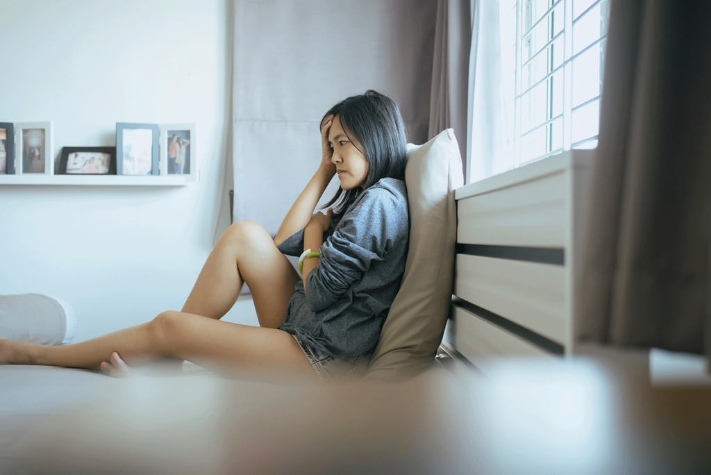 a woman living with ptsd sits in her bed and holds her hand to her forehead