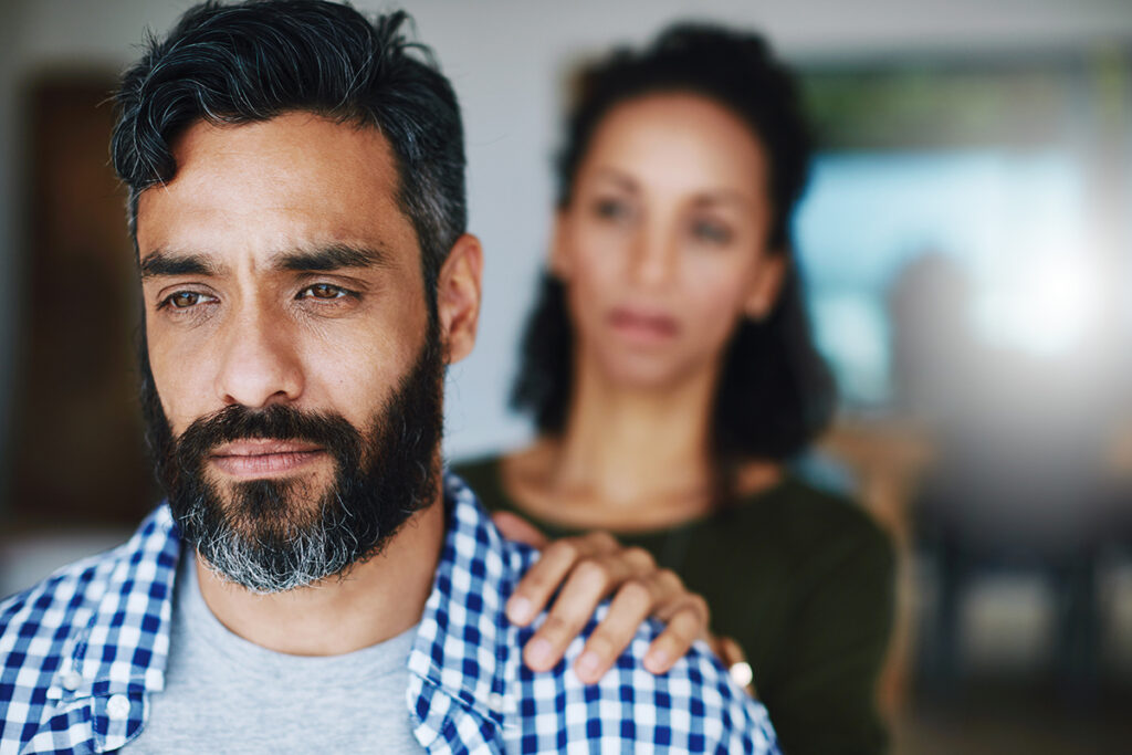 A woman has her hand on a man's shoulder. He is experiencing bipolar disorder.