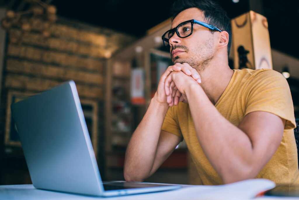 A man sits at his laptop with his hands clasped beneath his chin. He's pausing before responding to an email. He's learning to control his impulsivity.