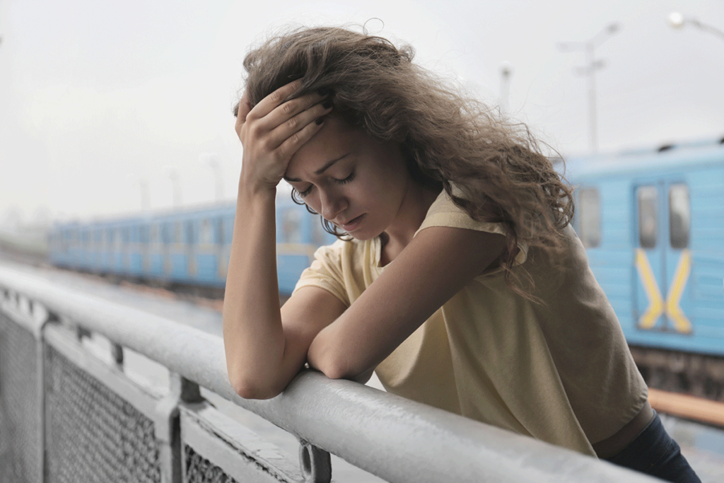 A woman is standing near a train and is holding her head in her hands. She is experiencing heroin side effects.