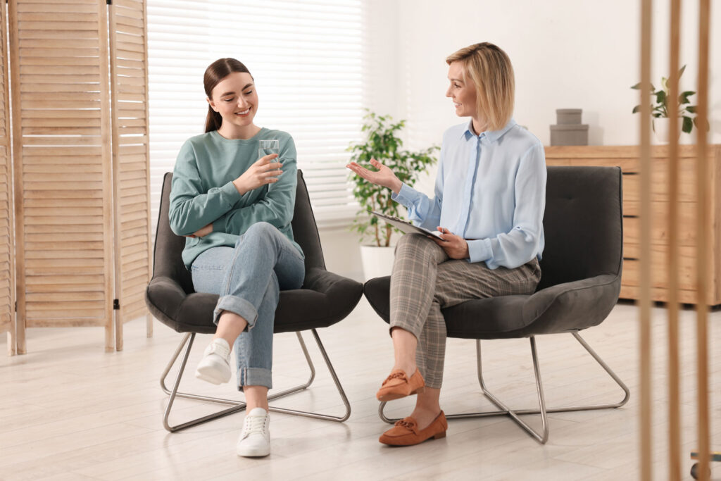 A young woman and her therapist are both smiling and enjoying talking about mental health.